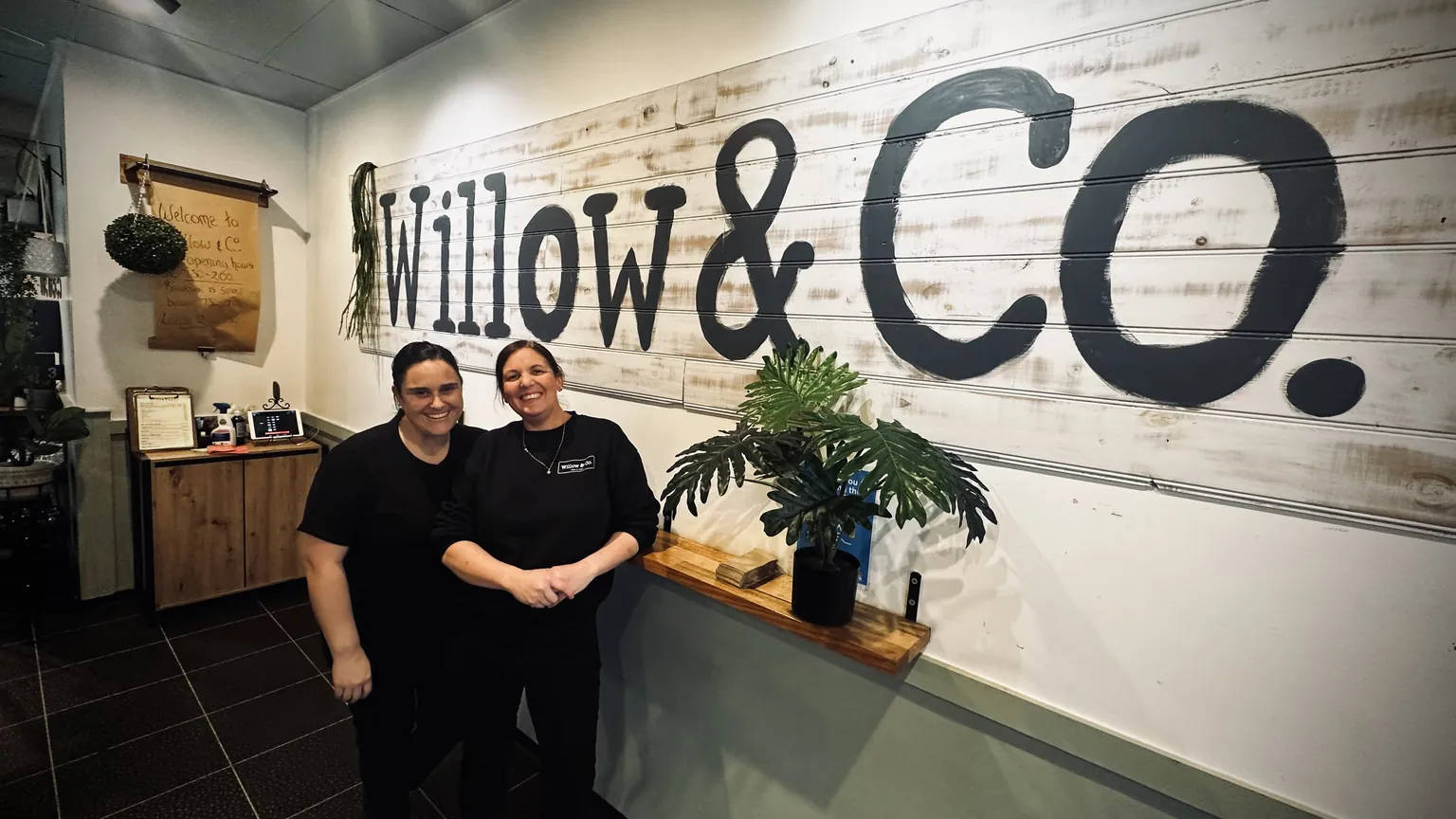The two owners of Willow & Co. standing in front of the hand-painted Willow & Co. sign that runs the length of the wall in their Albury coffee shop.